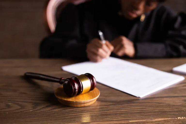 Russell Brand rape trial opens with predator claim in court Judge signing documents at desk with focus on gavel, representing law and justice